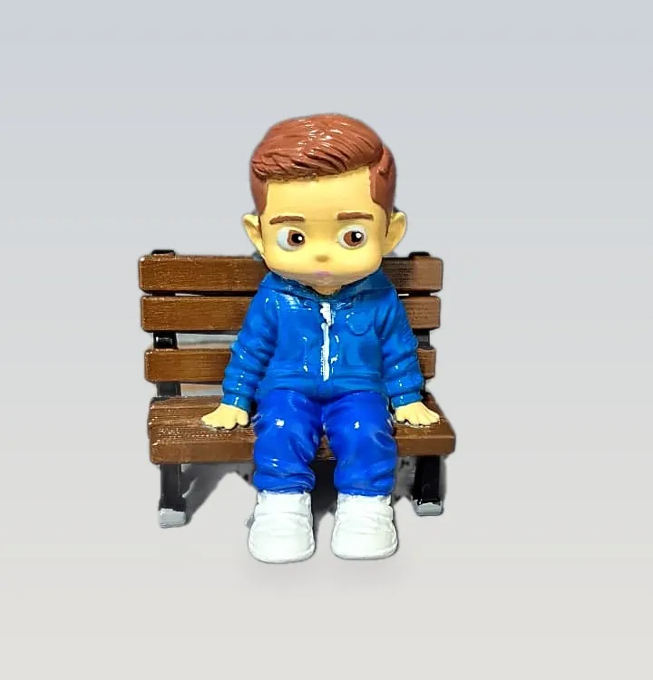 Boneco personalizado de um menino de agasalho azul sentado em um banco de praça em miniatura