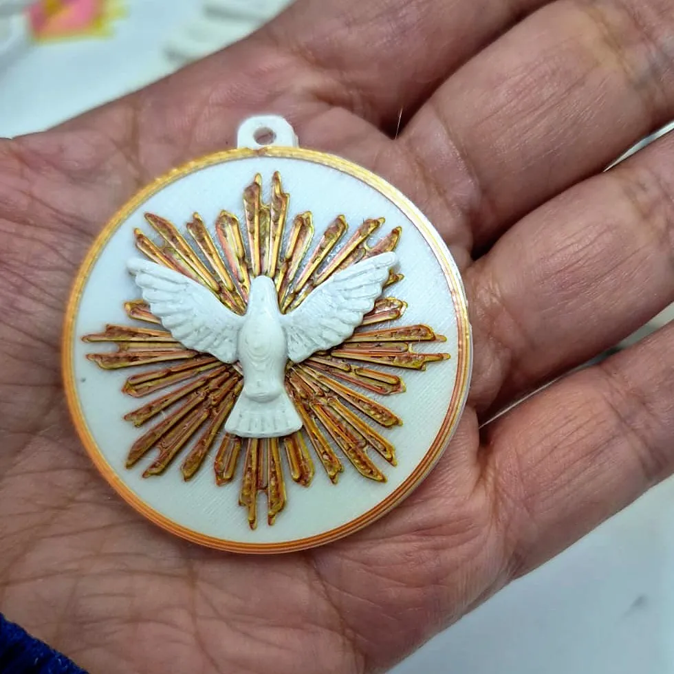 Medalha branca com pomba do Espírito Santo e raios dourados, na palma da mão, impressa em 3D pela JC3D