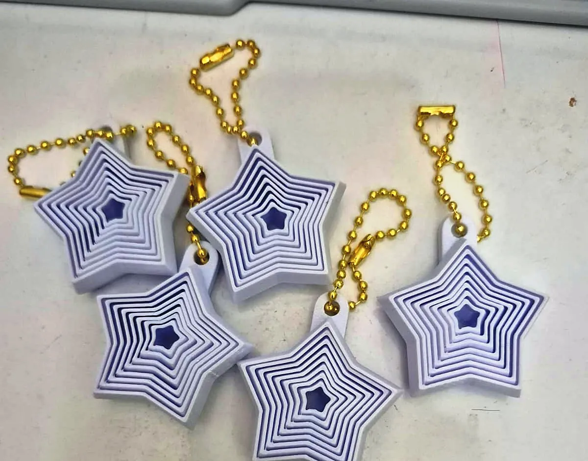 Cinco chaveiros em formato de estrela, brancos com camadas em relevo e miolo azul, com correntes douradas