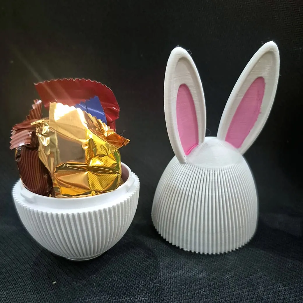 Ovo branco com orelhas de coelho aberto com chocolates dentro, ao lado da tampa, impresso em 3D pela JC3D