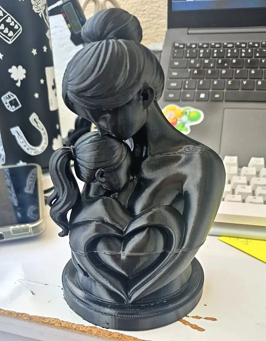 Escultura preta de uma mãe abraçando a filha, com coração vazado na base, impressa em 3D pela JC3D