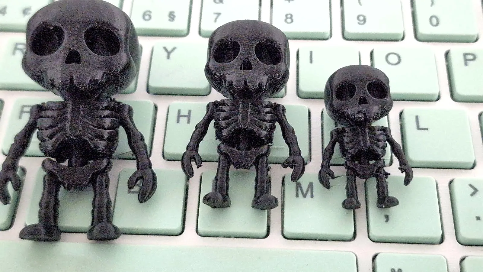 Três esqueletos pretos impressos em 3D, em tamanhos diferentes, sobre um teclado