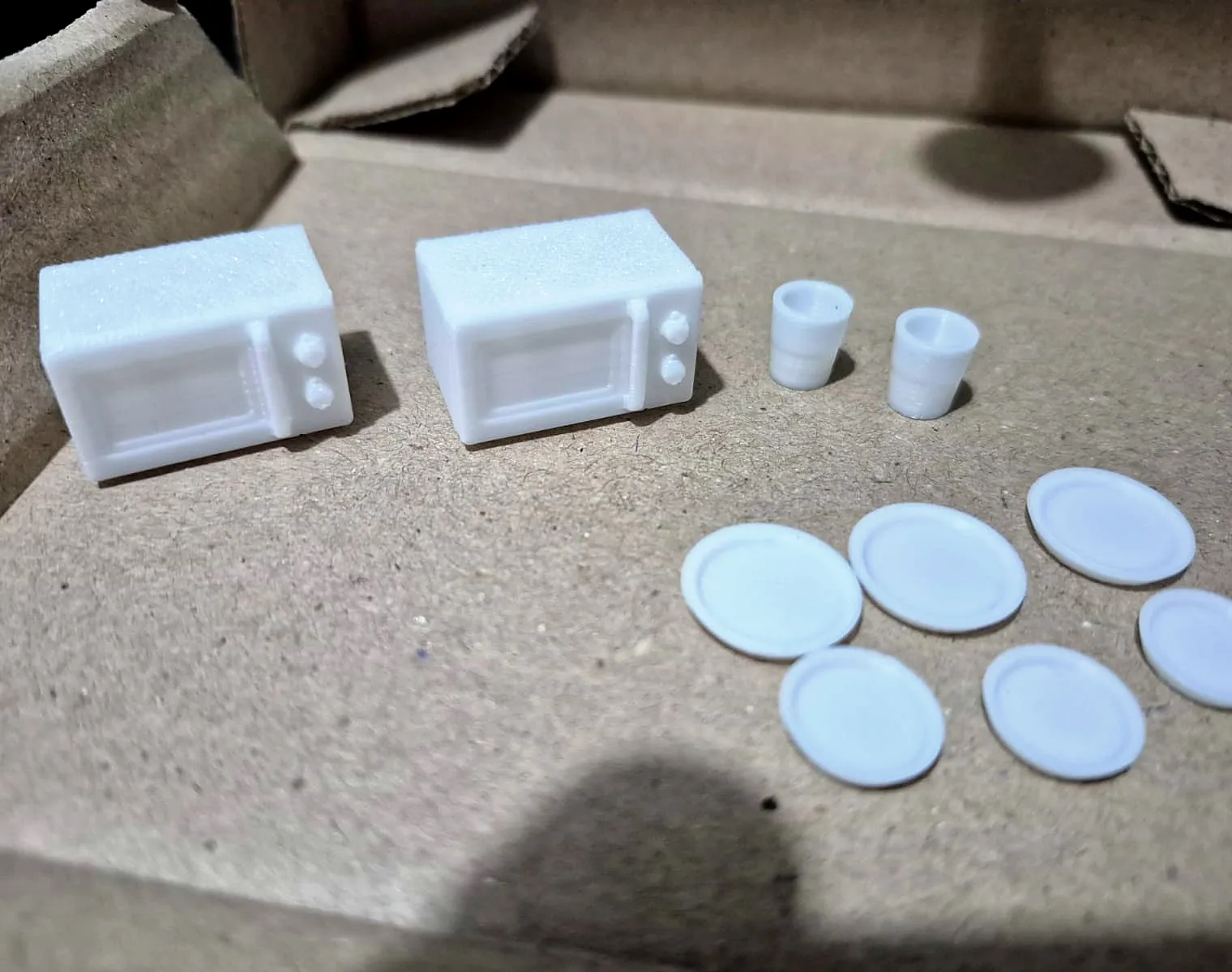 Dois micro-ondas, dois copos e seis pratos brancos em miniatura, impressos em 3D pela JC3D