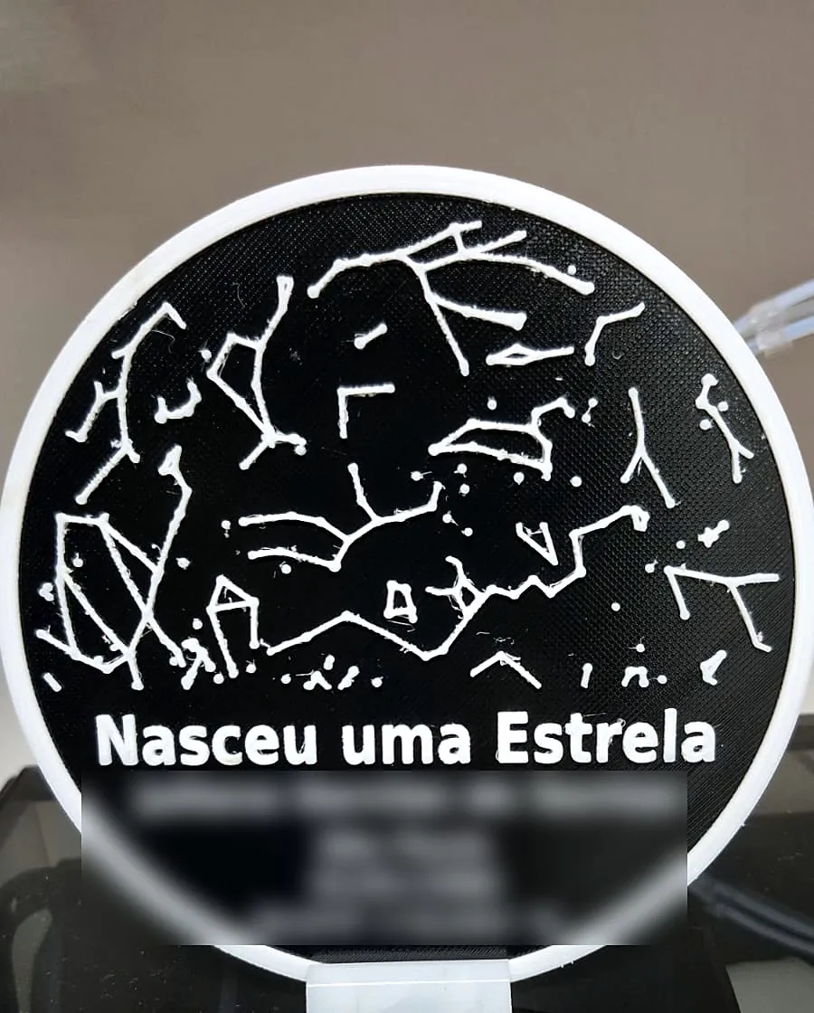 Placa redonda preta com mapa de constelações em branco e o texto Nasceu uma Estrela (nome, data e local desfocados)